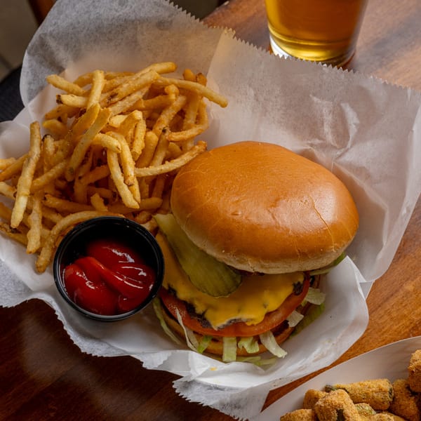 Cheeseburger with lettuce, tomato, and pickles, served with a side of fries and ketchup.