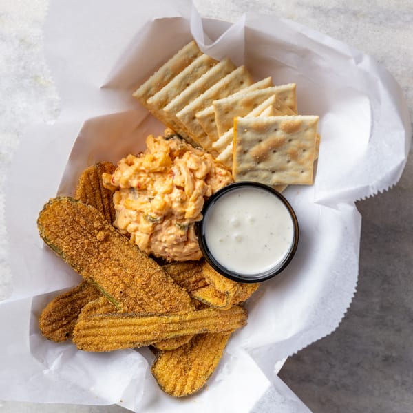 Fried pickles, pimento cheese, crackers, and ranch dressing in a white paper-lined basket.